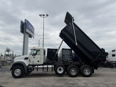 Mack GR64F dump truck in a dealership lot with its dump bed raised, side view shows white cab and multiple axles, VIN 1M2GR4GCXMM022853.
