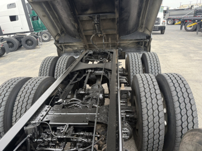 Truck chassis under dump bed showing drivetrain and rear axles with dual tandem setup.