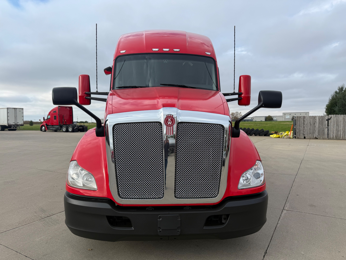 Front view of a red 2022 Kenworth T680 truck with large chrome grille, black bumper, and side mirrors.