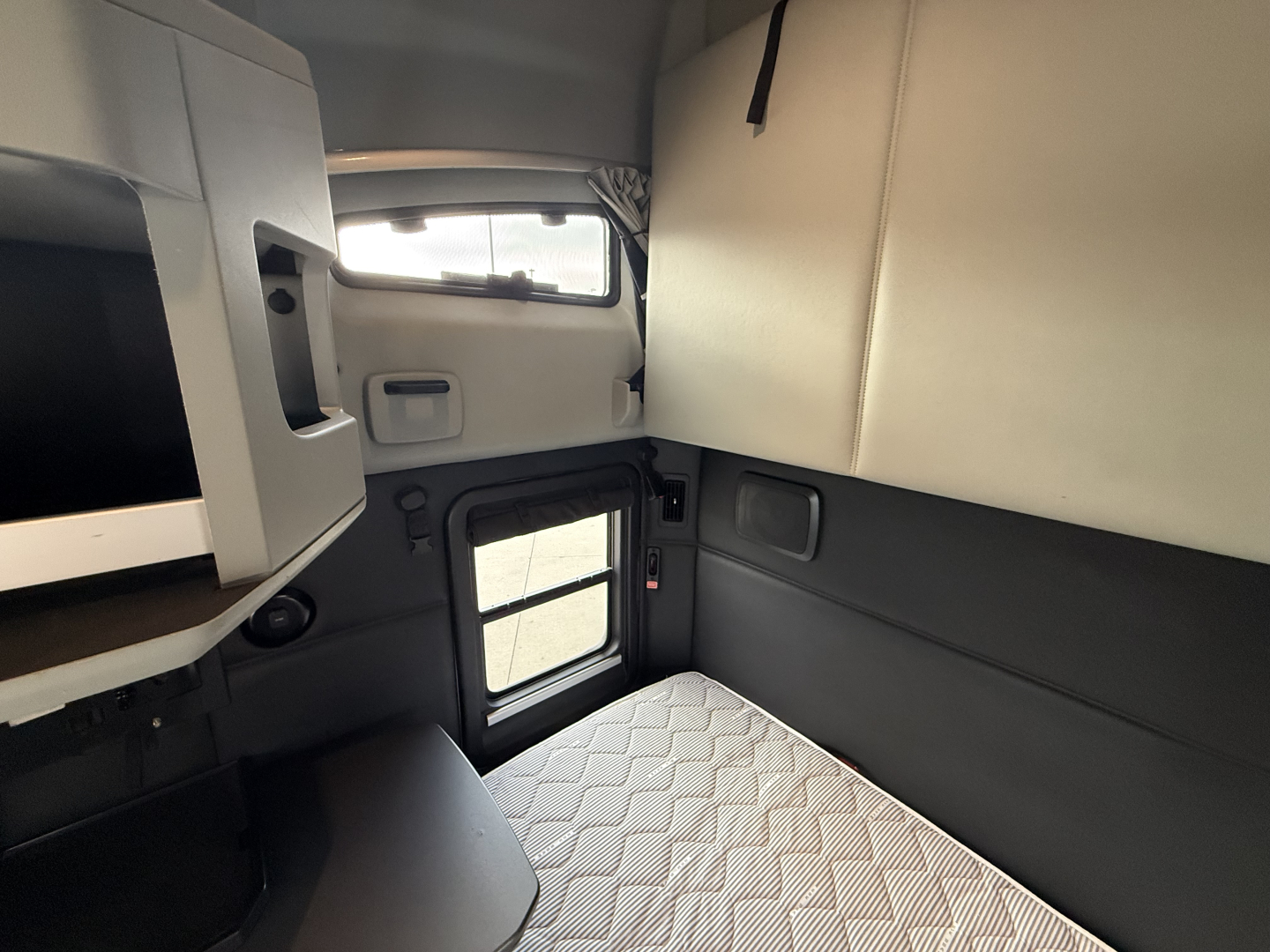 Kenworth T680 sleeper cab interior with platform bed and overhead storage, viewing small cabin window and door in view.