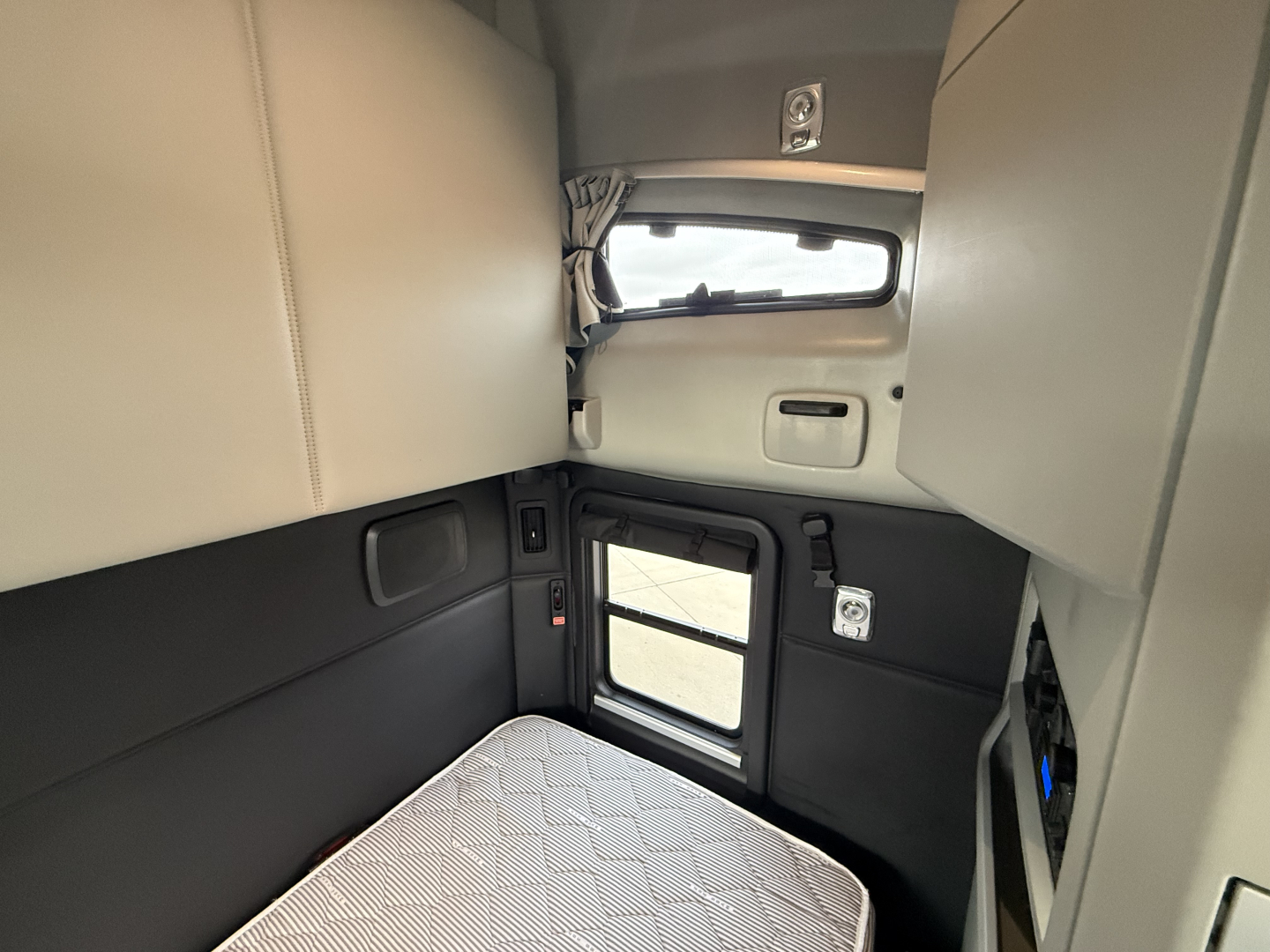 Kenworth T680 sleeper cab interior showing side window, bunk area, and storage panels. No visible branding text legible in image.