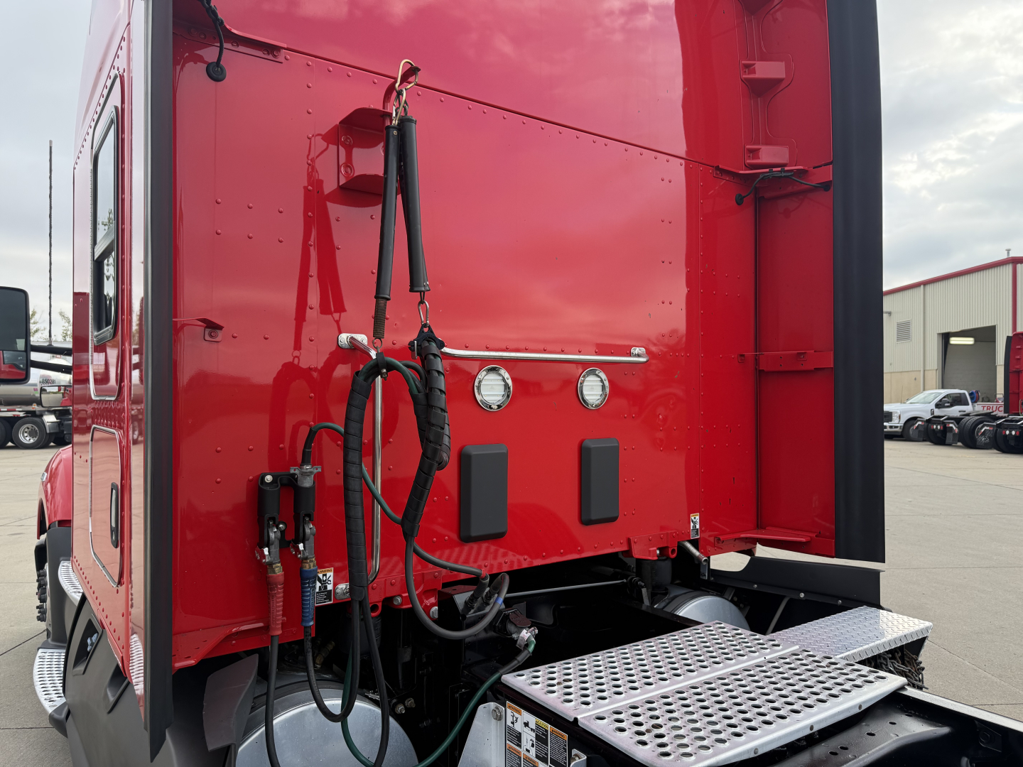 Kenworth T680 rear cab area showing ladder step and hookups with hoses and hardware in view.