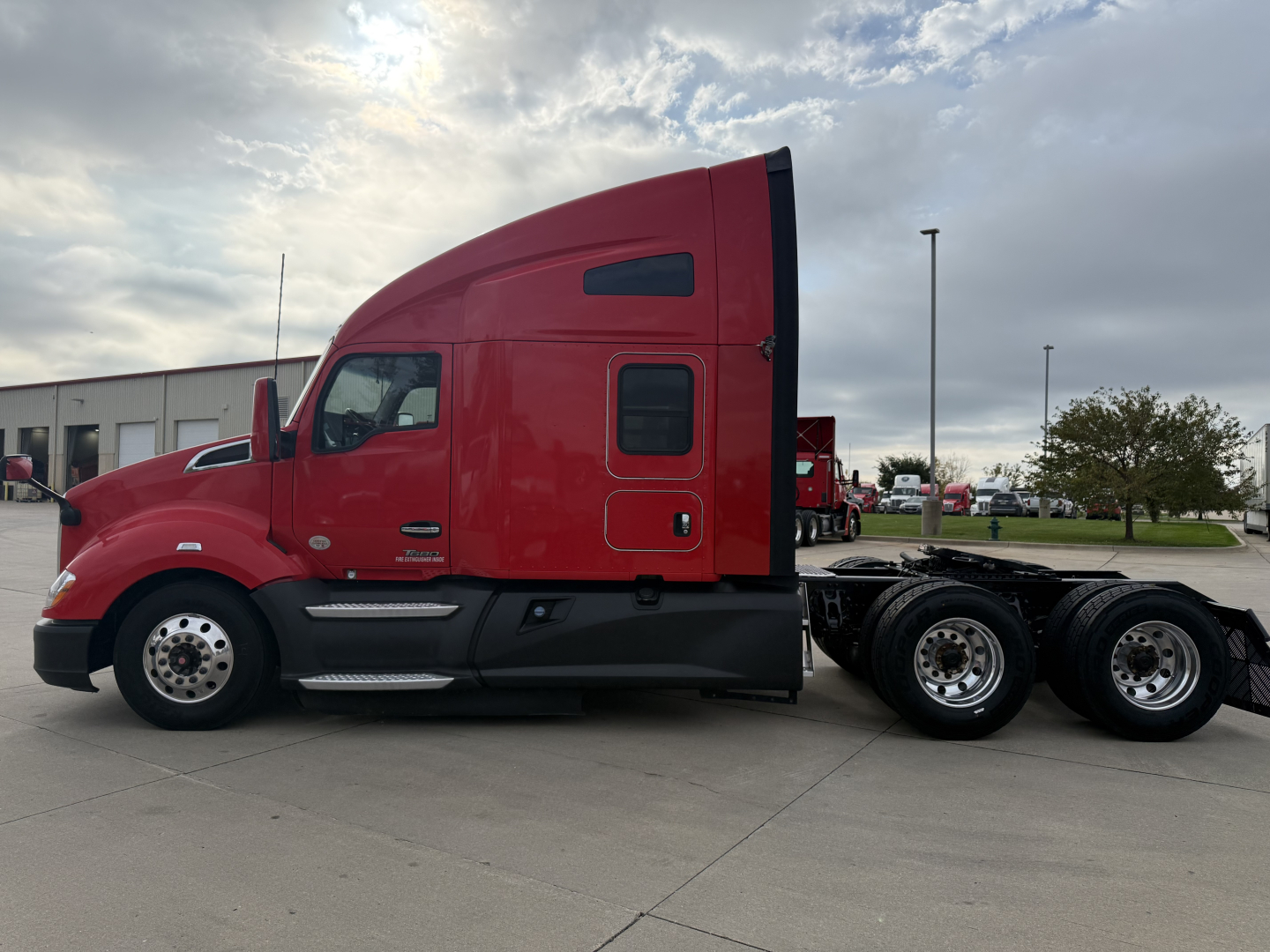 Kenworth T680 side view in red with sleeper cab and chassis showing fuel tanks and wheels.