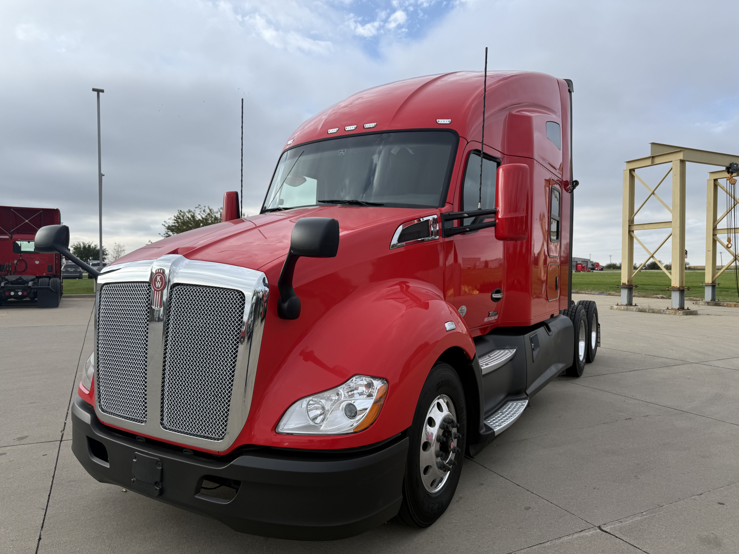 Kenworth T680 tractor in red parked, front-left view, chrome grille, dual fuel tanks, sleeper cab, May show VIN/stock label nearby