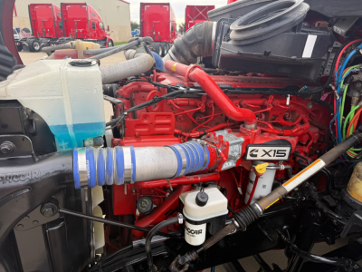 Kenworth T680 engine bay showing XE15 engine with red intake manifold, white coolant reservoir, blue silicone hose, and various hoses and wiring.