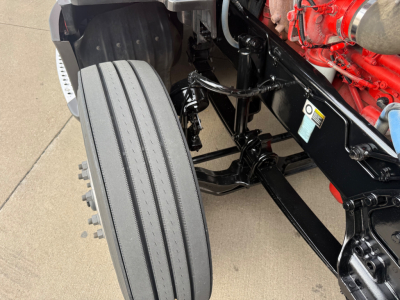 Kenworth T680 front wheel area and chassis with red engine block visible; features a large single front tire and black metal frame.