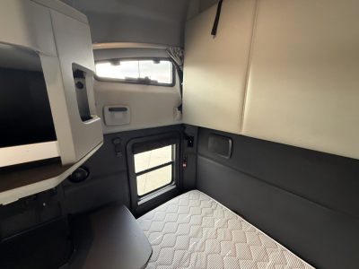 Kenworth T680 sleeper cab interior with platform bed and overhead storage, viewing small cabin window and door in view.