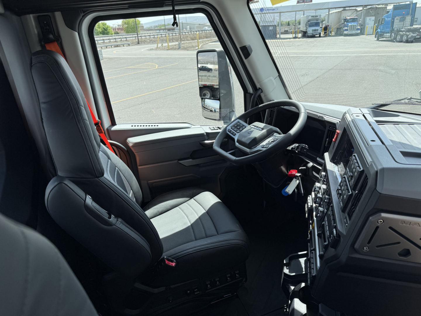 Truck cabin interior showing steering wheel, dashboard with controls, and driver seat of a 2027 Mack AN64T conventional daycab.