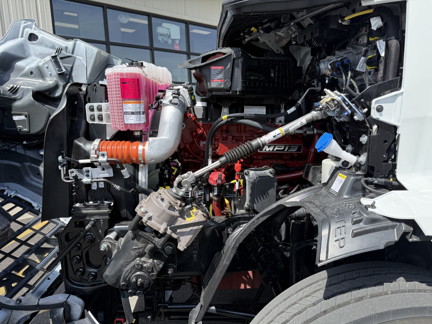 Truck engine bay showing large turbo and pink coolant reservoir with hoses and Mack MP engine label visible