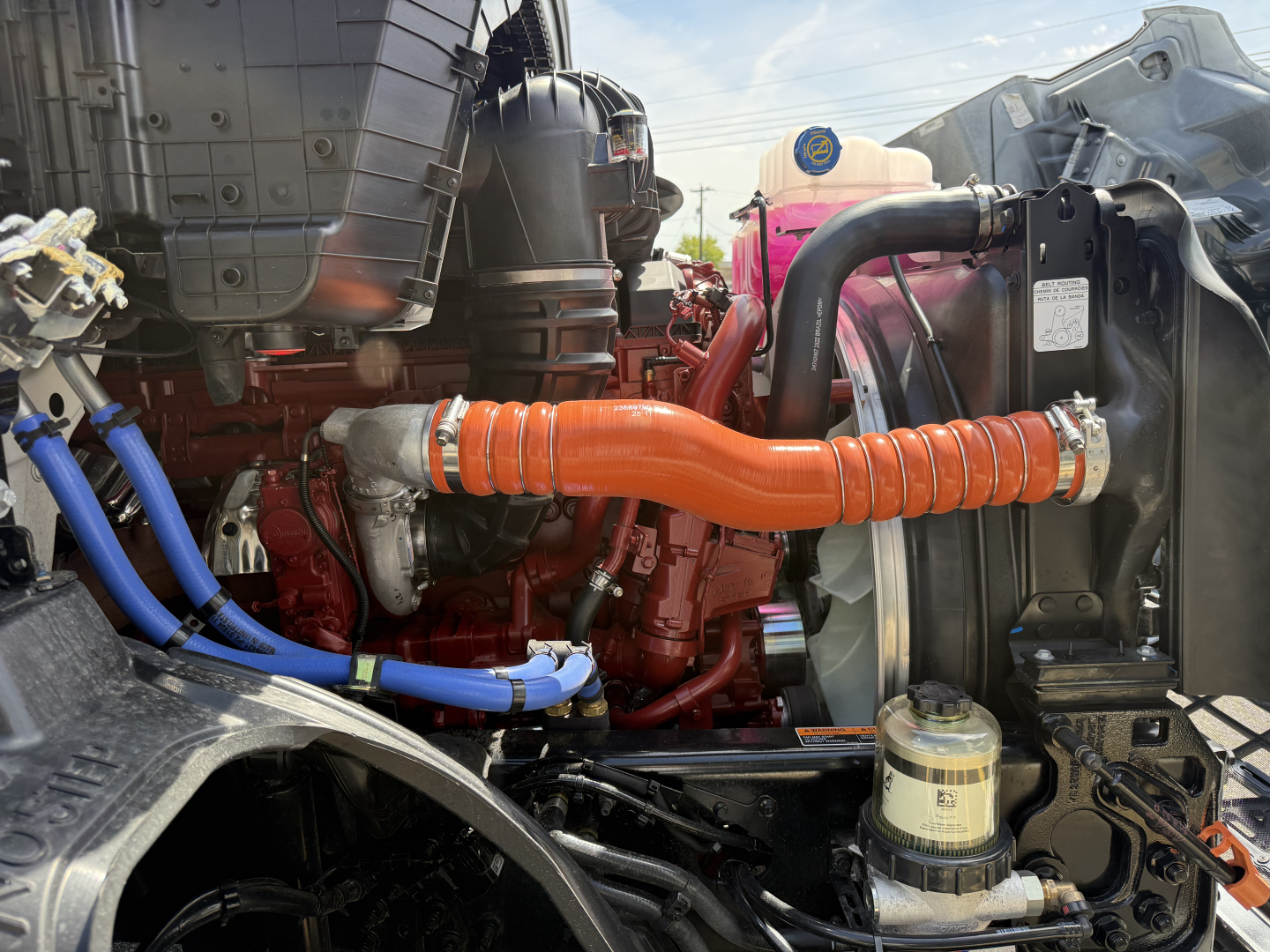 Mack AN64T engine bay showing orange flexible coolant hose, blue electrical harnesses, red engine block, and radiator assembly.