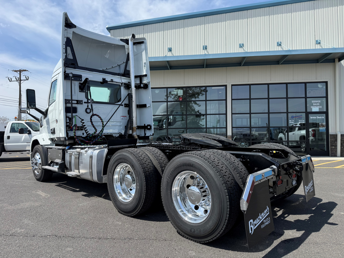 Mack AN64T conventional daycab truck in a dealership lot, side view showing rear dual axles, chrome wheels, and fifth wheel area; no visible text labels readable.