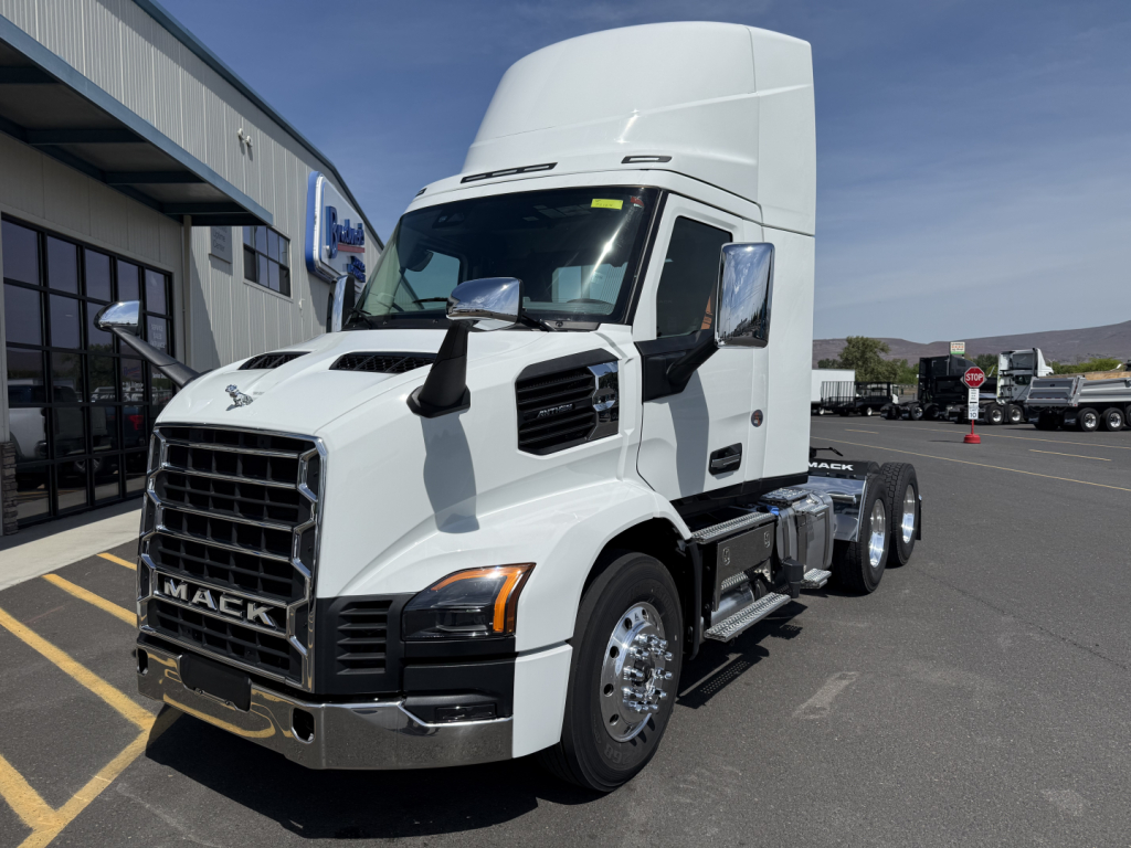 Truck cab exterior showing Mack AN64T conventional daycab with white paint and chrome grille, large side mirrors, and dual rear axles in a dealership lot.