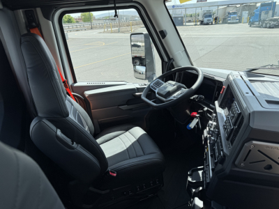Truck cabin interior showing steering wheel, dashboard with controls, and driver seat of a 2027 Mack AN64T conventional daycab.