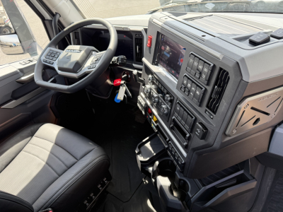 Mack AN64T cabin interior showing steering wheel, dashboard with large touchscreen, controls, gear shifter, and driver seat.