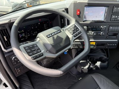Mack AN64T truck interior showing steering wheel with Mack logo, dashboard with digital gauges, control buttons on steering wheel, center console with touchscreen display.
