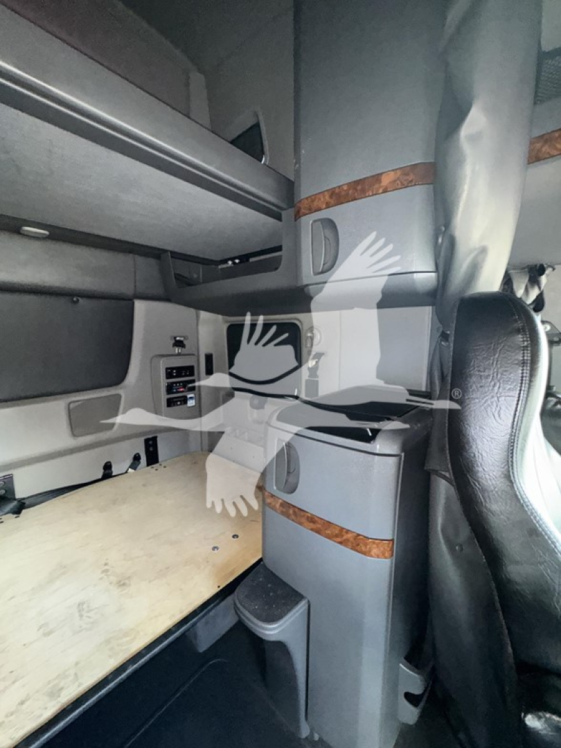 Cab interior of a 2019 International LT sleeper truck showing bunk area with storage drawers and wood trim; visible seat edge and side panel near dashboard.