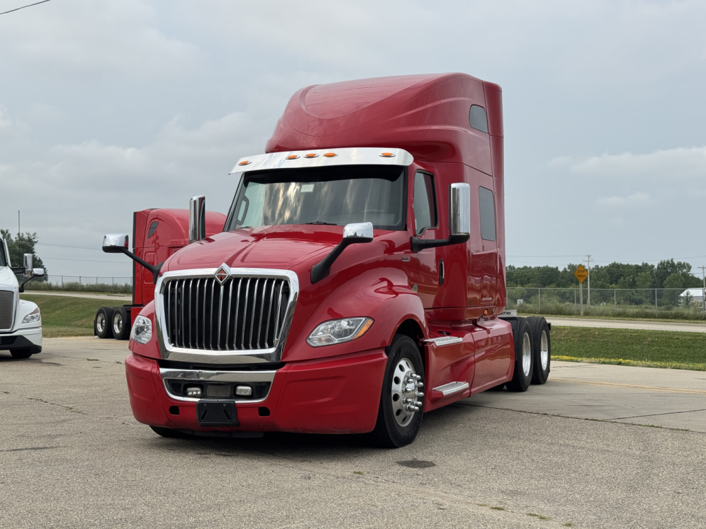 Tractor-trailer cab in red showing front grille, headlights, and aerodynamic sleeper, International LT model with elevated roof.