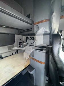 Cab interior of a 2019 International LT sleeper truck showing bunk area with storage drawers and wood trim; visible seat edge and side panel near dashboard.