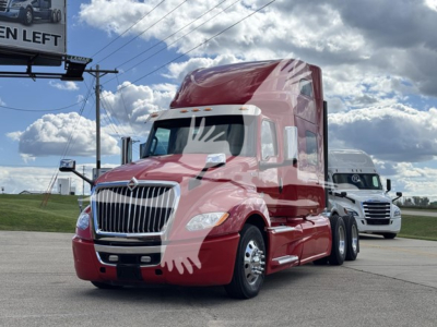 International LT truck in red with sleeper cab, front grille and headlights visible, on a highway lot.