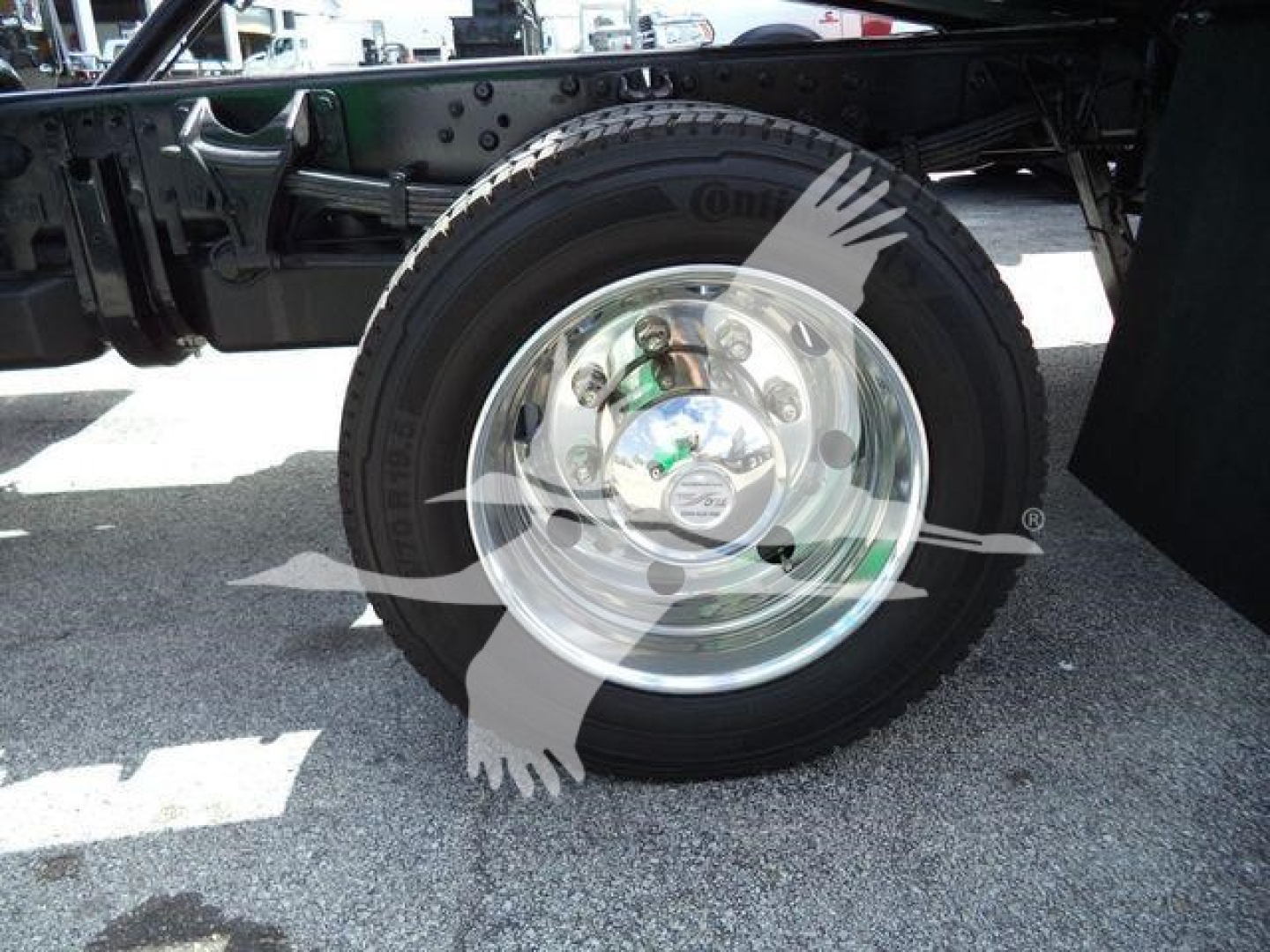 Wheel and tire assembly on truck frame showing shiny steel rim and hub with bolts.