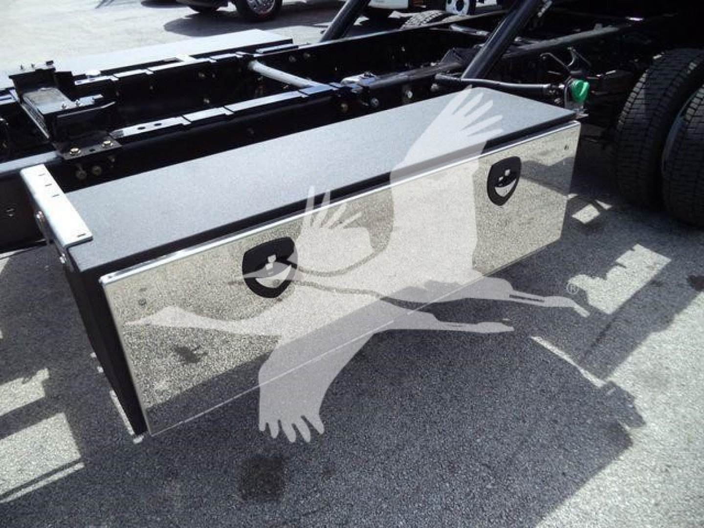Black aluminum toolbox mounted on a truck frame with two circular latches and reflection of a bird logo