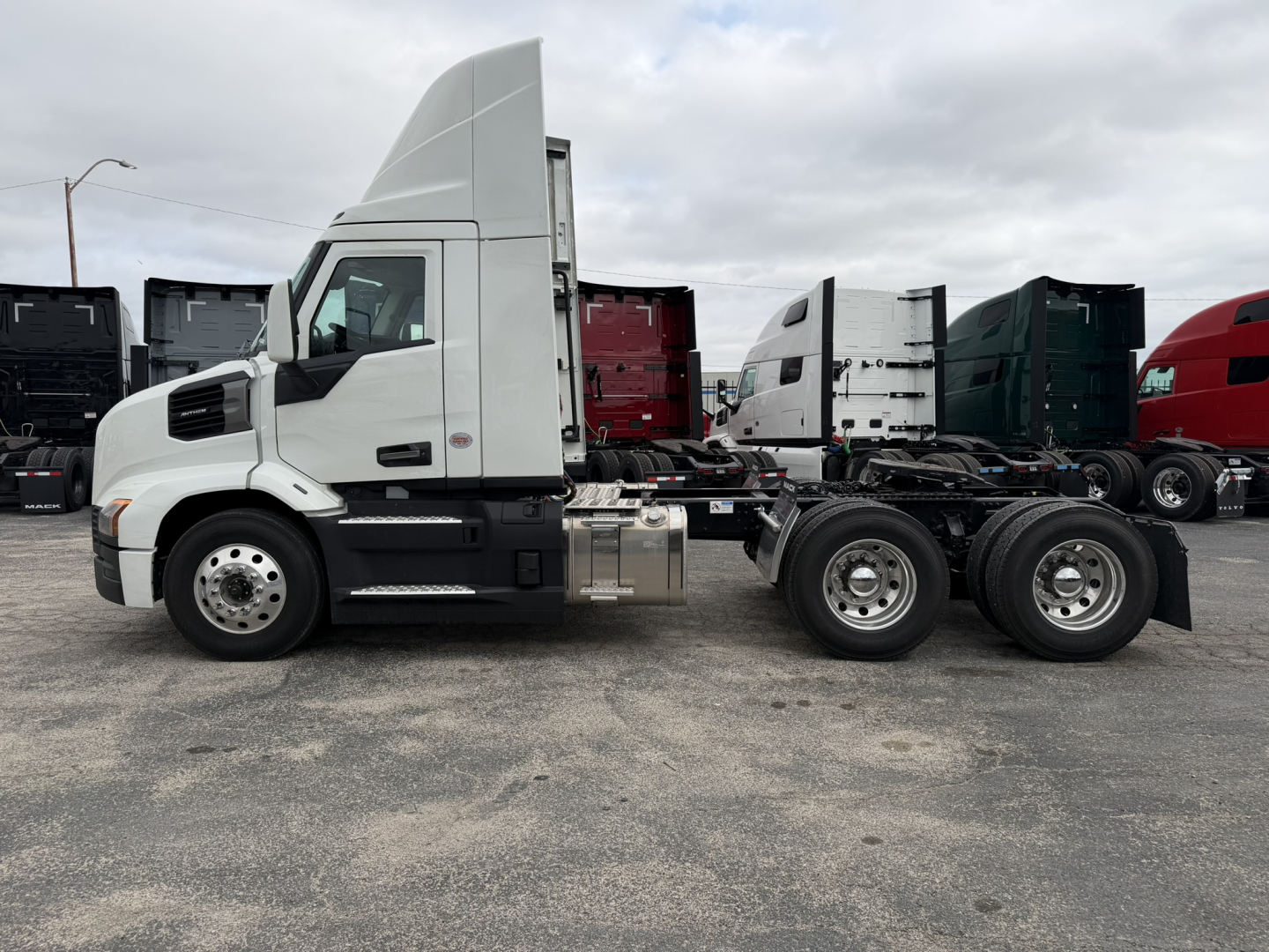 Truck side view showing a white 2027 Mack AN64T conventional daycab chassis with sleeper cab, fuel tanks, and dual rear axles.
