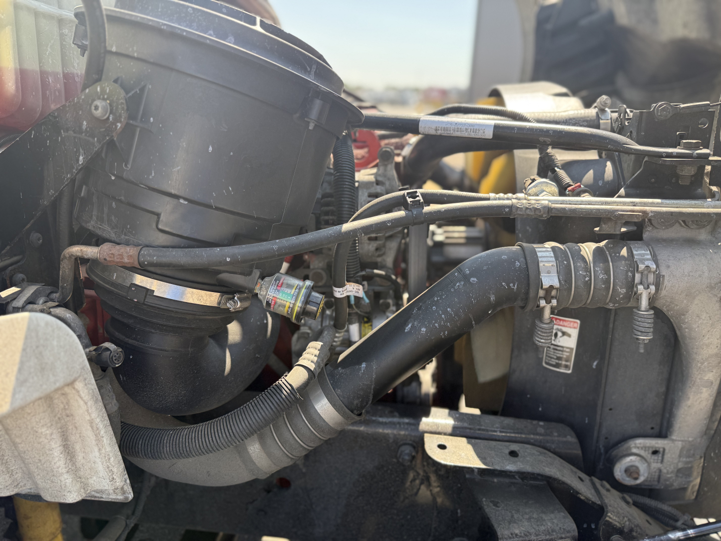 Freightliner M2106 engine bay showing air intake housing, hoses, and exhaust connections with visible clamps and fluid lines.
