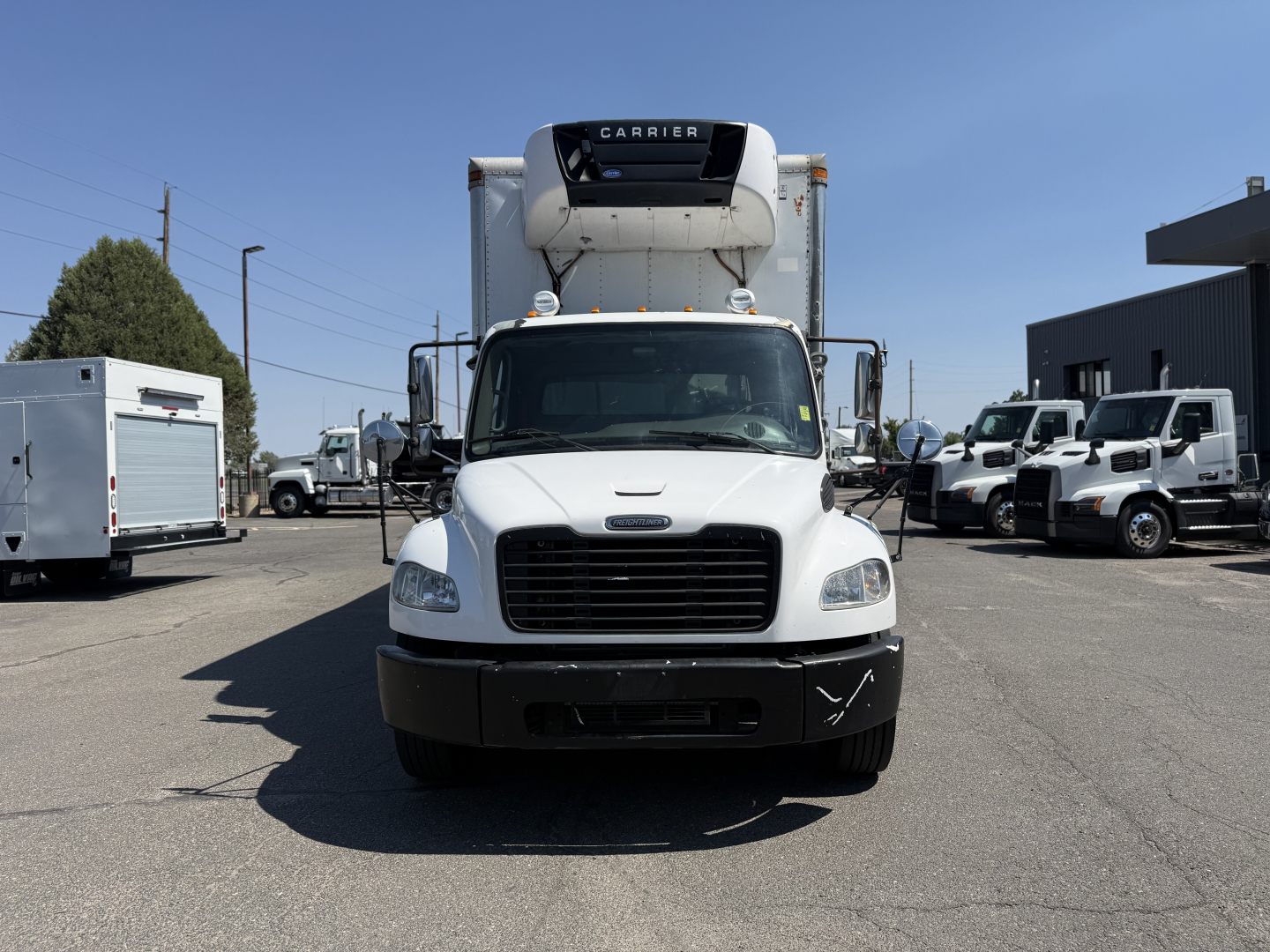 Front view of a white 2008 Freightliner M2106 refrigerated truck with Carrier unit on the roof, black bumper, and surrounding trucks in a dealership lot.