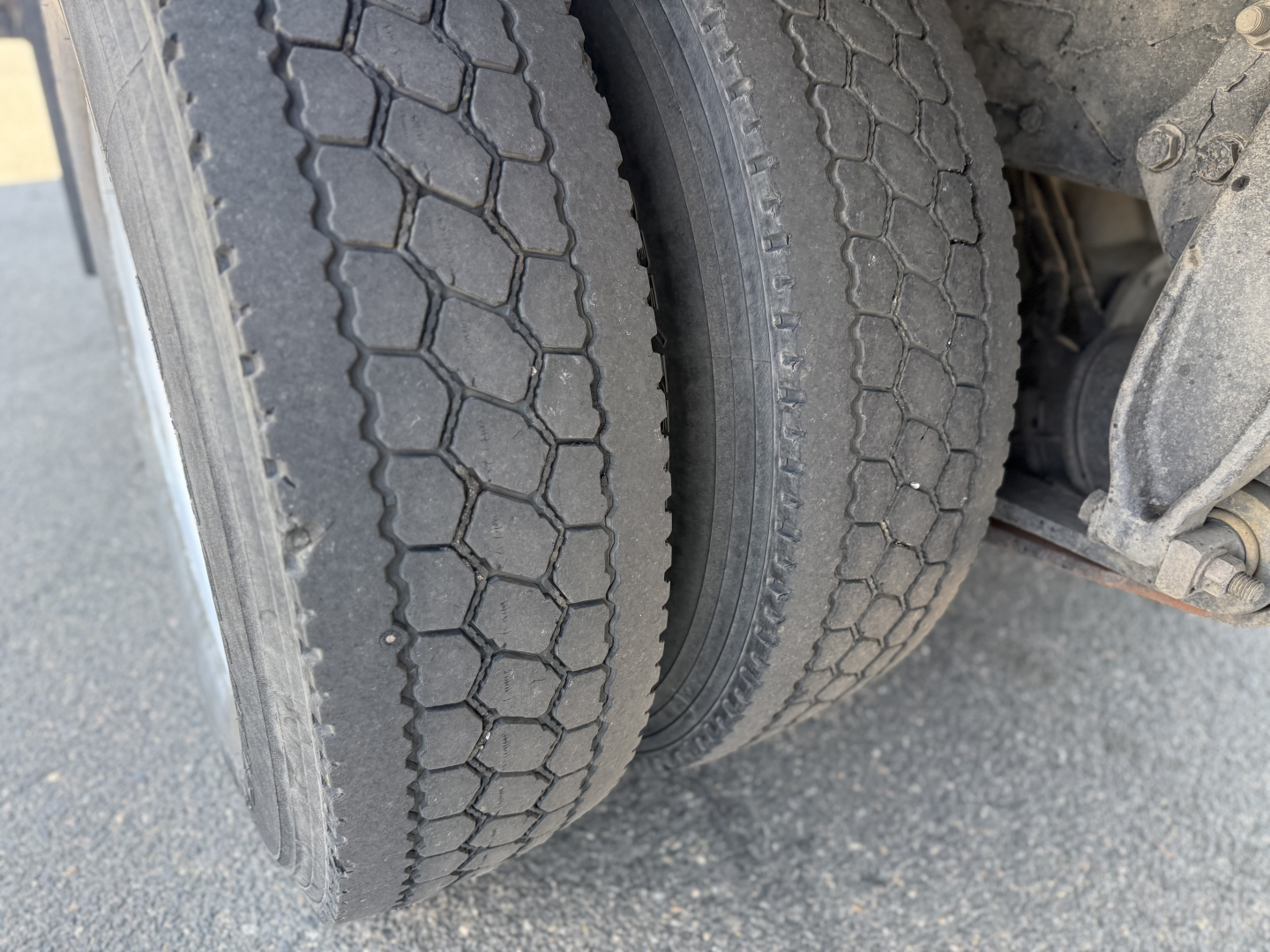 Rear dual tires of a Freightliner truck axle with textured tread and wheel well visible.