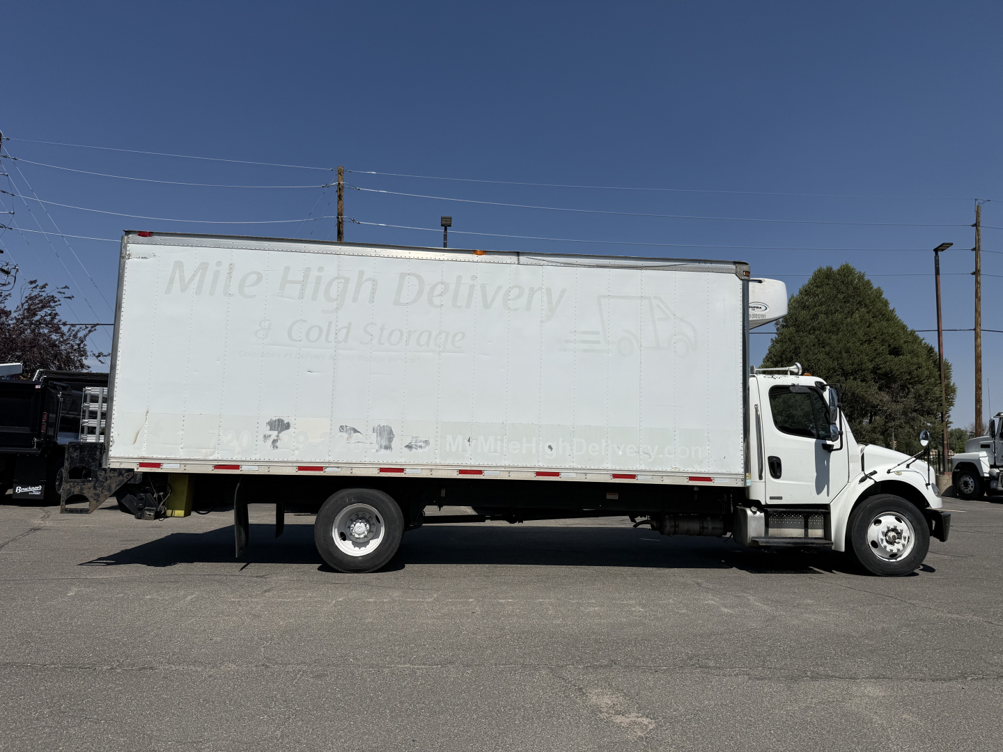 Freightliner M2106 refrigerated box truck side view showing Mile High Delivery logo on cargo area and white cab, VIN 1FVACWDT28DZ72341 visibility text not legible.