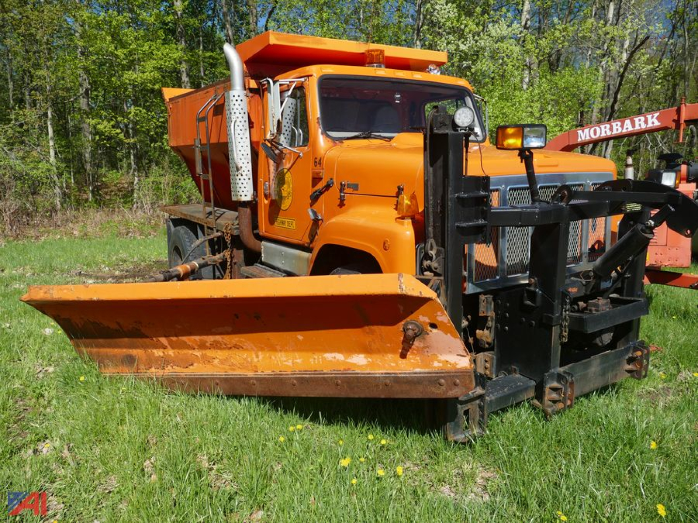 International 2574 truck with a large snow plow/sander attachment in field, orange color, cab visible, snow removal equipment on front