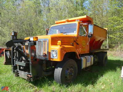 International 2574 dump truck with sander and wing, orange in-service vehicle, front view showing snow plow attachment and side cab details.
