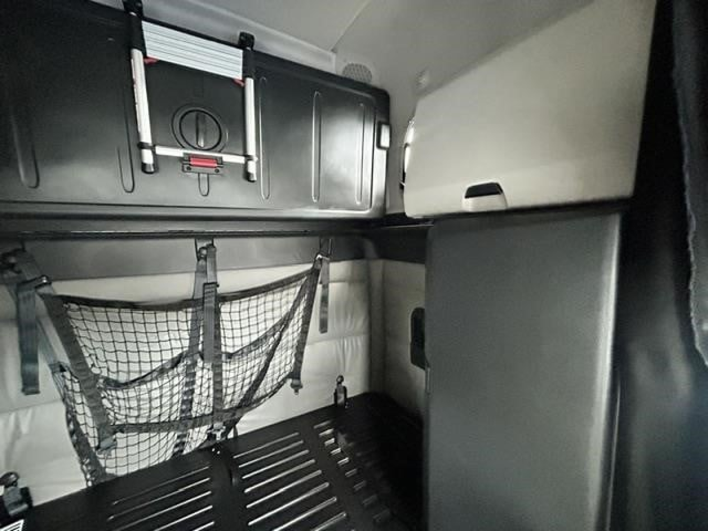 Conventional sleeper truck cab interior showing storage compartments, overhead luggage rack, and netting securing items.