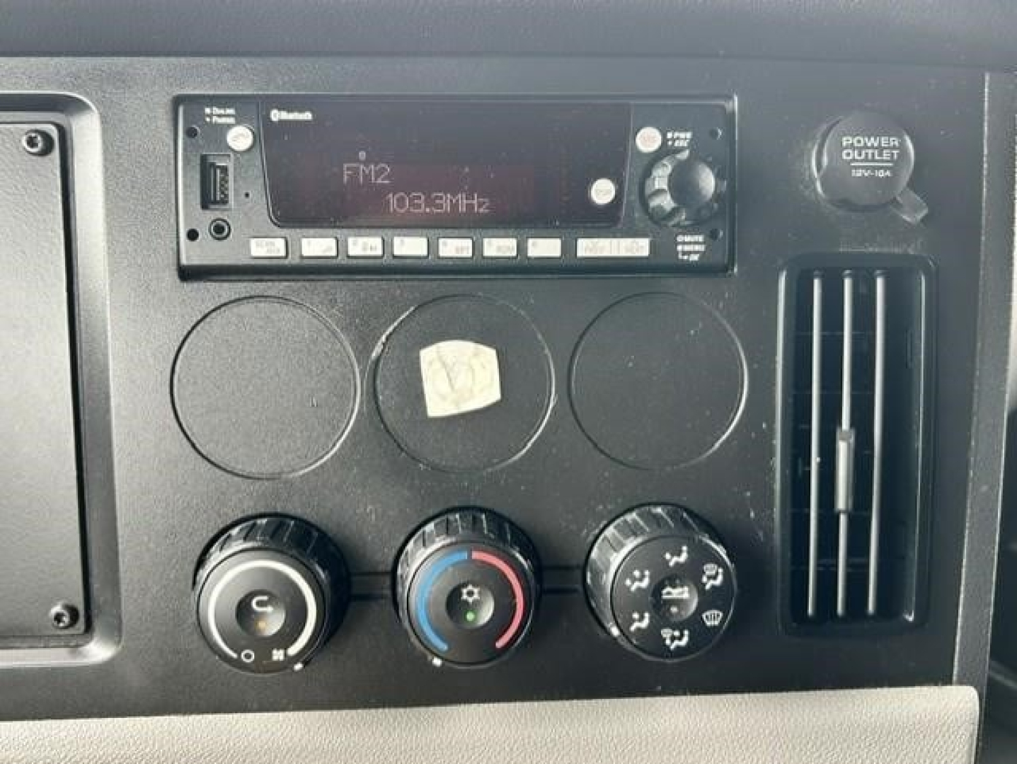 Dashboard of a 2022 Freightliner Cascadia 126 showing FM2 radio display 103.3MHz, three control knobs, and a power outlet vent panel.