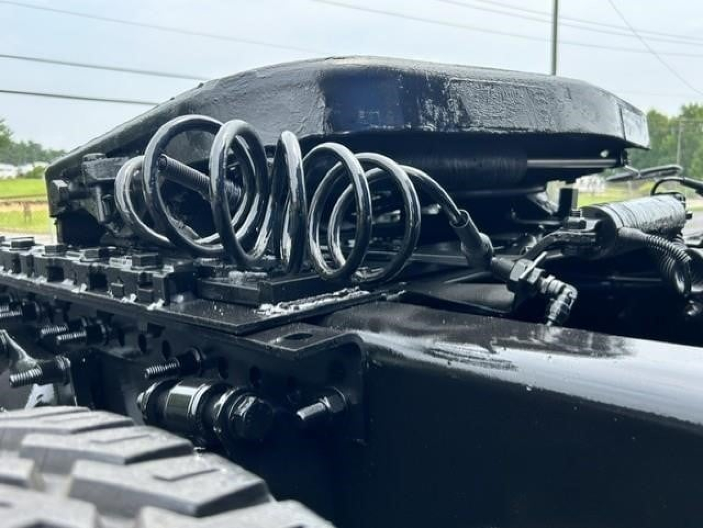 Tractor-trailer fifth wheel area showing coiled airline hoses and mounting hardware on a Freightliner Cascadia chassis rail.