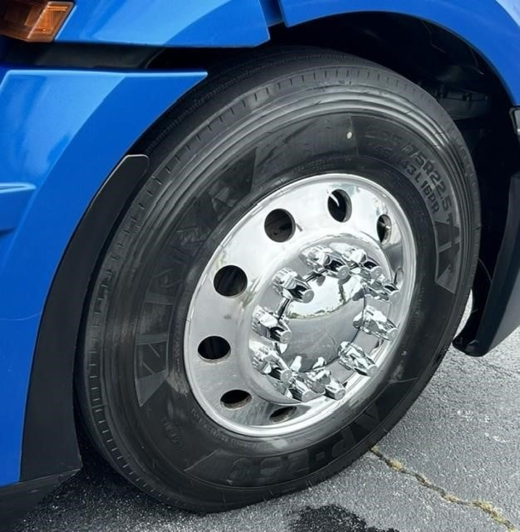 Truck front wheel area of a blue 2022 Freightliner Cascadia 126 showing a polished chrome hub, black tire, and partial fender