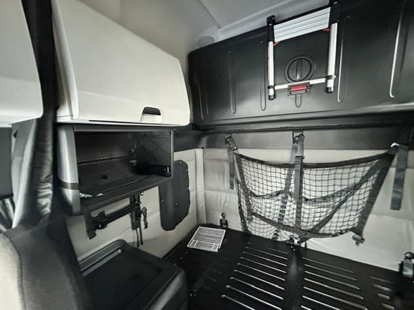 Freightliner Cascadia sleeper cab interior showing storage nets and overhead cabinets with a folded ladder rack and cargo area.
