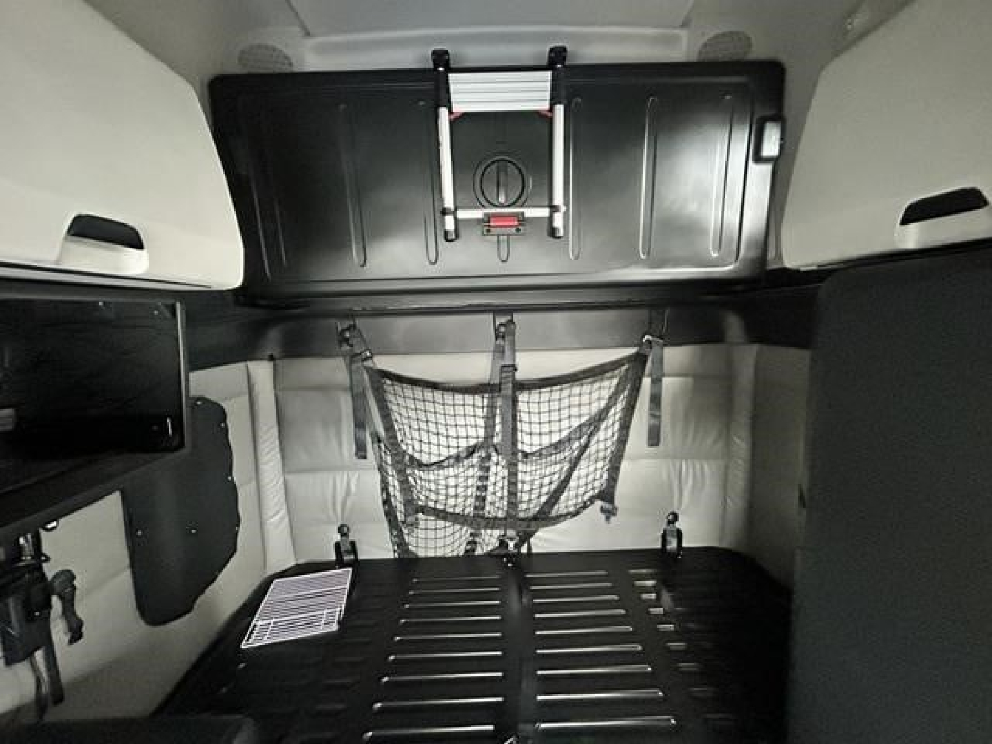 Freightliner Cascadia sleeper cab interior showing storage net, overhead panel, and cargo area with black bed and side panels.