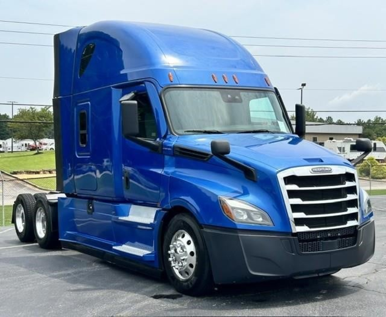 Truck cab showing a blue Freightliner Cascadia 126 with sleeper, chrome wheels, and dual rear axles; front grille and headlights visible.