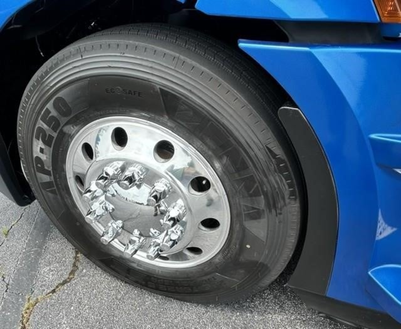 Truck wheel: front left tire on a 2022 Freightliner Cascadia 126, with shiny steel rim and tire brand P250 visible, blue cab in background.