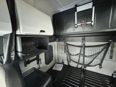 Freightliner Cascadia sleeper cab interior showing storage nets and overhead cabinets with a folded ladder rack and cargo area.