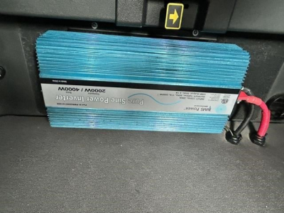 Blue blue-sleeved power inverter/rectifier unit mounted under dash with label; text includes 2300W 3000W input? (Note: exact text not fully legible) showing electrical module, wires with red/black connectors.