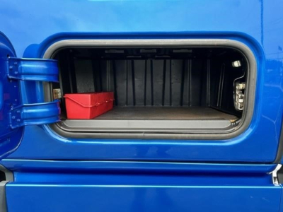 Truck exterior storage compartment showing open side fuel/air tank hatch with a red tool box inside.