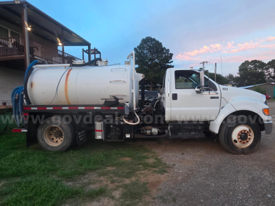 Ford F-750 vacuum truck side view showing cylindrical tank and cab, with loader and hoses visible.