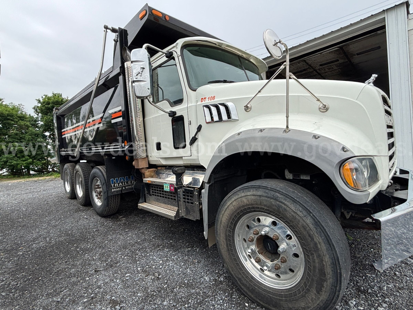 2020 Mack Granite dump truck in-service showing front cab, large chrome grille, DT-126 engine badge, side steps, and dump body with black and orange stripes.
