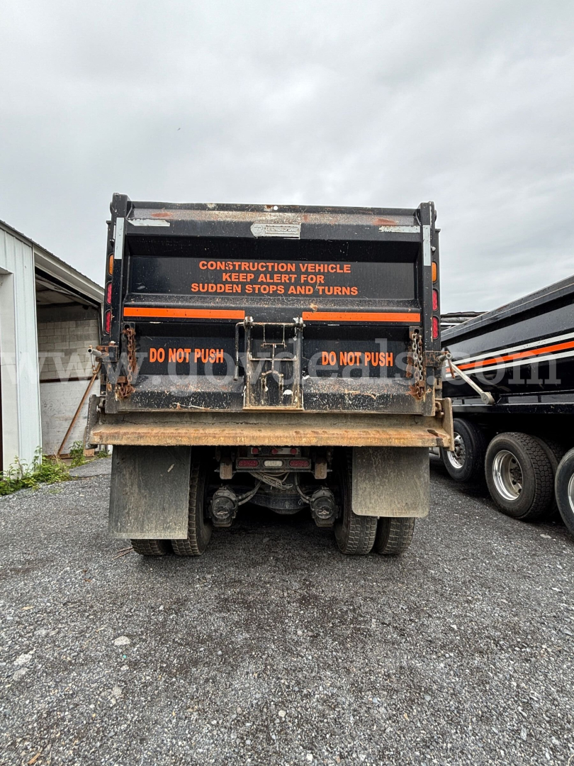Rear view of a 2020 Mack Granite dump truck showing warning decals, mud flaps, and hydraulic mechanism beneath the bed.