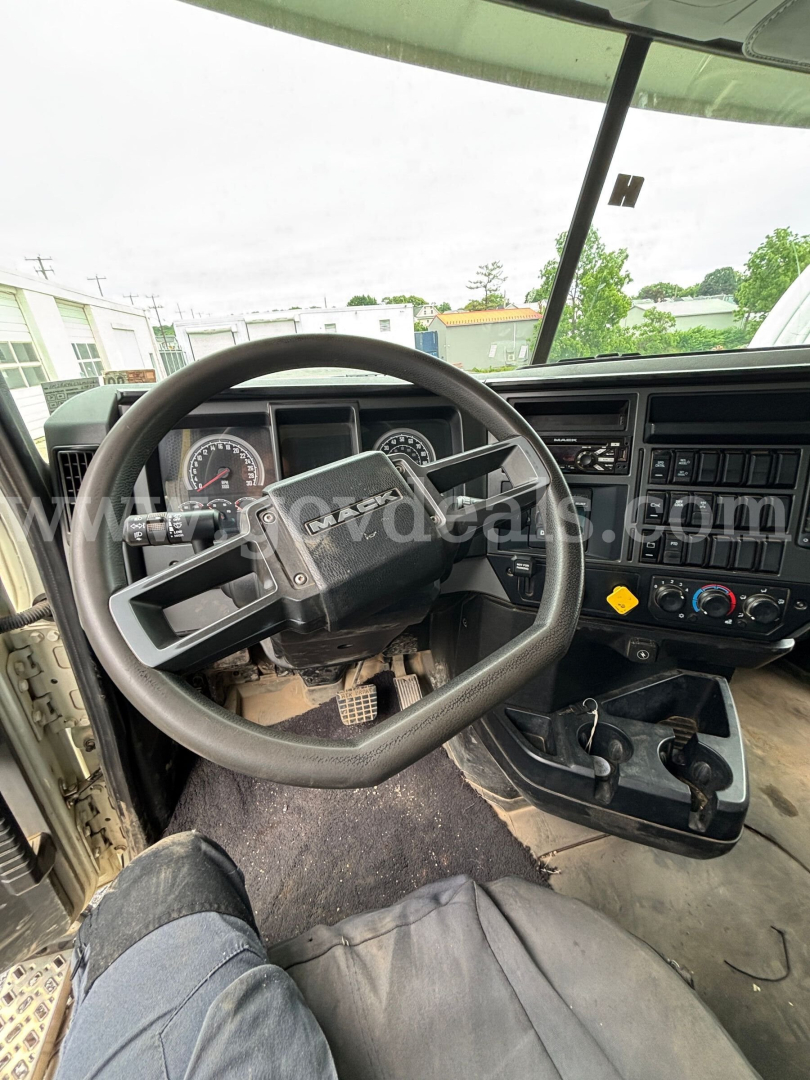 Truck cab interior of a Mack Granite showing steering wheel, dashboard with gauges, gear shifter, and center console; visible pedals and driver seat.