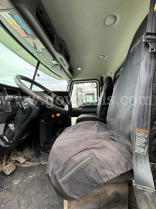 Truck cab interior of a 2020 Mack Granite in-service showing driver seat with seat cover, steering wheel, dashboard, and entry area.