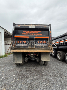 Rear view of a 2020 Mack Granite dump truck showing warning decals, mud flaps, and hydraulic mechanism beneath the bed.