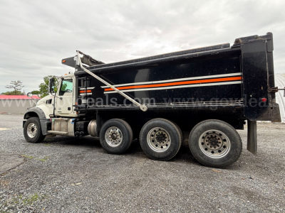 Truck side view showing a black Mack Granite dump truck with orange and white stripes, chrome cab mirrors, and six wheels; no legible model text visible on the image.